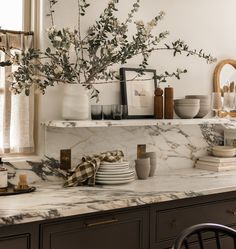 a kitchen counter with plates and cups on it, next to a vase filled with flowers