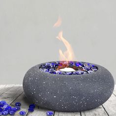 an outdoor fire pit with blue glass pebbles around it and a lit candle in the center