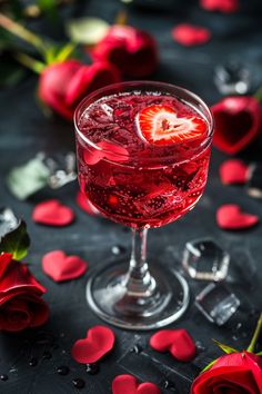 a glass filled with liquid next to red roses and petals on a black tablecloth