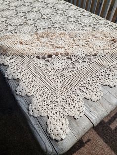 the table is covered with crocheted doily and sits on an old wooden bench