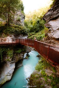 people are standing on a red bridge over a blue river in the middle of a canyon