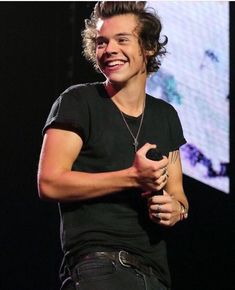 a smiling young man holding a microphone in his right hand and wearing a black t - shirt