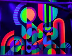 an abstract painting with bright colors and shapes on the wall in front of a dark background