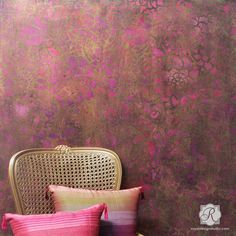 a chair sitting in front of a wall covered in pink and gold paint with two pillows on it