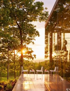 an outdoor dining area with glass walls and wooden flooring, overlooking the forest at sunset