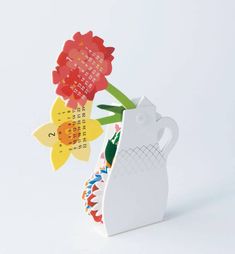 a white vase with flowers in it on a table next to a calendar card holder