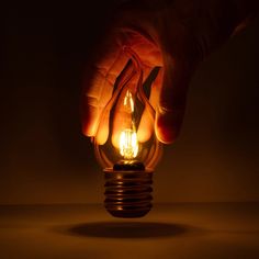 a person holding a lit light bulb in their left hand, on a dark background