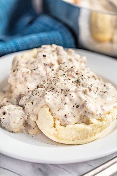 an english muffin topped with cream sauce on a white plate next to a fork