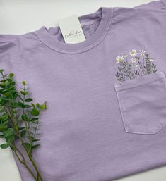 💐The perfect spring/summer tee!  These beautiful embroidered wildflower pocket tee's are soft, comfortable, and will make great gifts....or keep for yourself!    💐Pocket embroidered design: Featuring Wildflowers and Daises T-Shirts are available in a variety of colors: Pepper, Banana, Light Green, Berry, Blossom, Chambray, Orchid, Ivory, and Bay Brand: Comfort Colors Garment Dyed  Sizes: Adult Unisex S - 3XL Relaxed Fit 6.1 oz. 100% ring-spun cotton Garment dyed for that lived in feel and almo Spring T-shirt With Pockets And Relaxed Fit, Cute Crew Neck Top With Pockets, Embroidered Tops For Everyday Spring Wear, Spring Embroidered Top For Everyday Wear, Embroidered Cotton Lavender Top, Embroidered Lavender Cotton Top, Spring Relaxed Fit T-shirt With Pockets, Relaxed Fit T-shirt With Pockets For Spring, Lilac Shirt