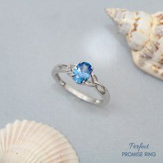 a ring with a blue topaz sits next to a seashell on a gray surface