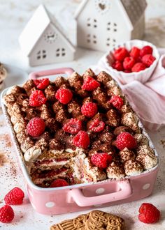 a cake with raspberries on top in a pink box next to some cookies