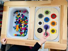 a child is holding up a wooden tray with different colored beads in it and an open box on the floor