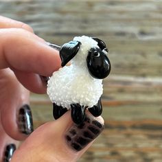 a hand holding a small toy sheep in it's left hand with black and white fur