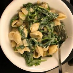 a white bowl filled with pasta and spinach on top of a black countertop