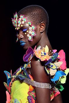 a woman with flowers on her face and hair in front of a black background, wearing an elaborate head piece