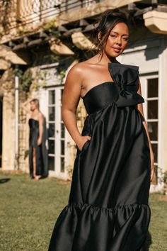 a woman standing in the grass wearing a black dress