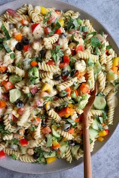 a bowl filled with pasta salad next to a wooden spoon on top of a table