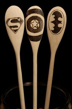 three wooden spoons with designs on them sitting in a glass container next to each other