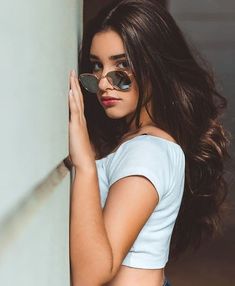 a woman wearing sunglasses leaning against a wall