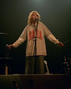 a woman standing in front of a microphone on stage with her arms out to the side