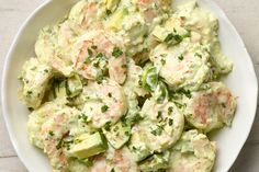 a white bowl filled with cucumber and shrimp salad on top of a table