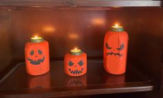 three pumpkin jars with candles in them sitting on a shelf