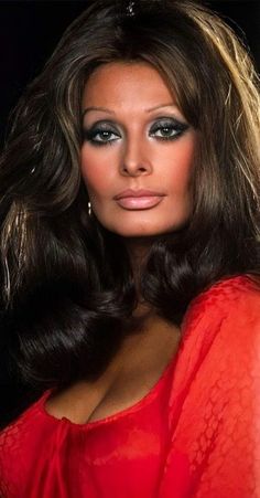 a woman with long brown hair and blue eyeshadow wearing a red dress posing for the camera