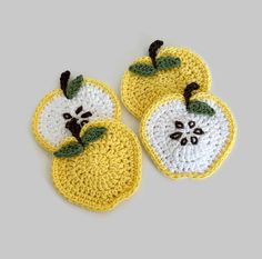 two crocheted apples with green leaves on them, one is yellow and the other is white