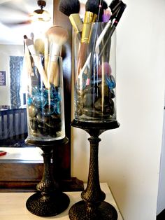 two vases filled with makeup brushes on top of a table