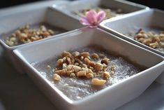 three square trays filled with food on top of a table next to a pink flower