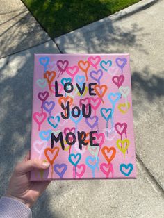 someone is holding up a card that says love you more with hearts painted on it