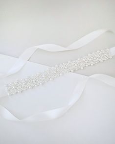 a bridal sash with pearls and satin ribbon on it's side, sitting on a white surface