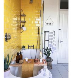 a yellow tiled bathroom with a tub, shower head and plants in the bathtub