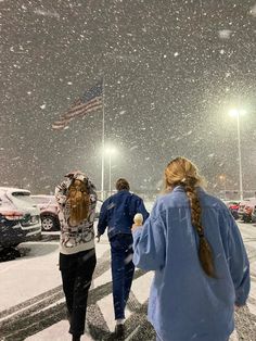 three people walking in the snow at night with an american flag flying high above them