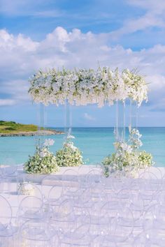 an outdoor wedding setup with white flowers and clear acrylic chairs on the beach