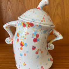 a ceramic teapot with multicolored dots on it sitting on a wooden table