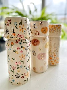 four glass jars sitting on top of a table next to a potted plant in the background