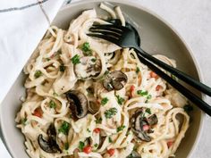 a bowl filled with pasta and mushrooms on top of a white table cloth next to a fork