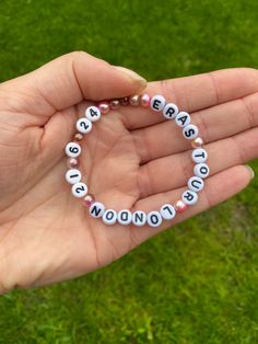 a hand holding a beaded bracelet with words written in white and pink beads on it