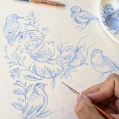 a person is drawing flowers and birds on paper