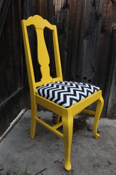 a yellow chair with a black and white seat cover on the back is sitting in front of a wooden fence