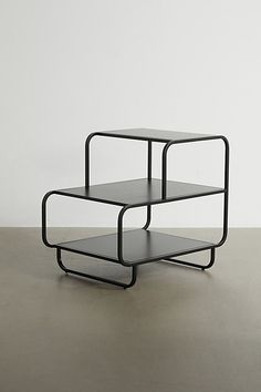 three tiered black metal side tables against a white wall, with one shelf stacked on top of the other