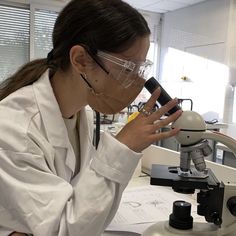 a woman in white lab coat looking through a microscope