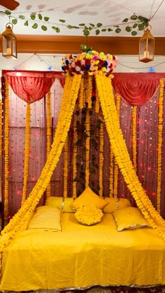 a bed covered in yellow flowers next to red drapes and hanging lights on the ceiling