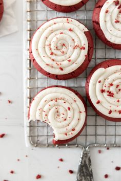 red velvet cookies with white frosting and sprinkles on a cooling rack