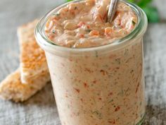 a glass jar filled with food sitting on top of a table next to crackers