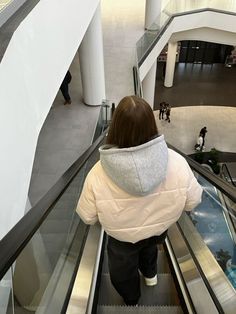 a woman riding an escalator down the middle of a shopping mall while wearing a white coat