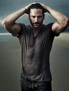 a man is standing on the beach with his hands in his hair and looking at the camera