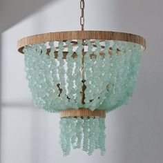 a chandelier made out of glass beads hanging from a wooden frame with a light fixture in the background