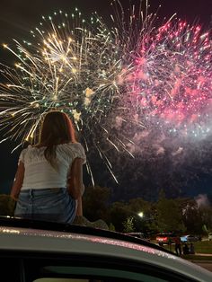 a woman standing on top of a car looking at fireworks